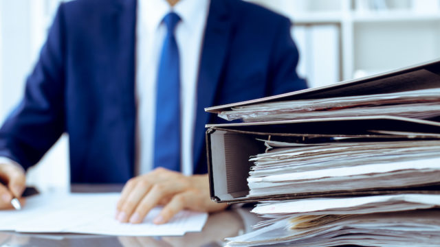 Binders with papers are waiting to be processed with businessman back in blur. Accounting planning budget, audit, insurance and business concept