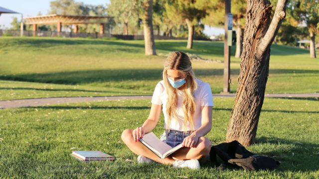 A student wearing a face mask studying outside.