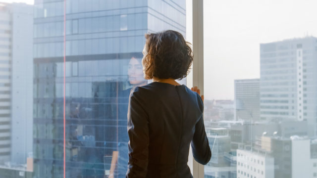 Shot of the Successful Businesswoman in a Stylish Dress in Her Office Looking out of the Window Thoughtfully. Modern Business Office with Personal Computer and Big City View.