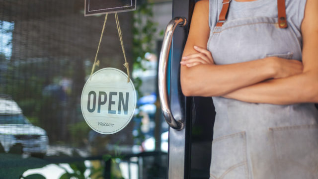 The woman is a waitress in an apron, the owner of the cafe stands at the door with a sign Open waiting for customers. Small business concept, cafes and restaurants.